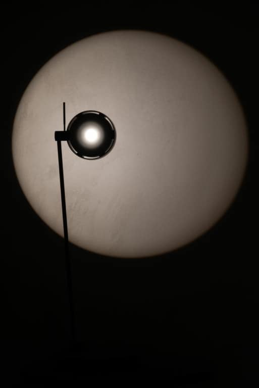 Minimalistische Design-Stehleuchte erzeugt kreisförmigen Lichtschein auf dunkler Wand – Beispiel für gezielte Lichtwirkung und atmosphärische Lichtgestaltung.